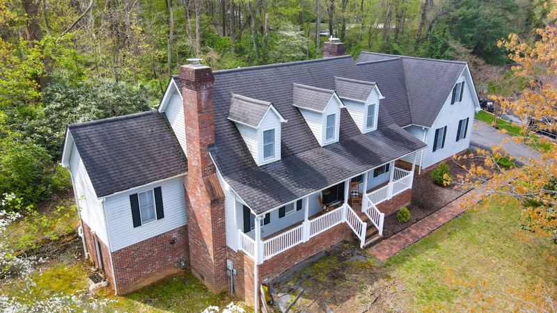 Drone aerial of a two-story home with a wraparound porch surrounded by trees